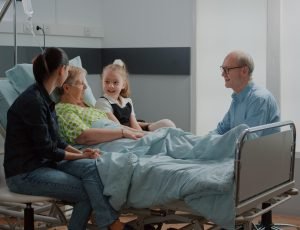 Niece hugging sick woman at family visit in hospital ward, child and mother visiting retired patient with disease. Hospitalized person enjoying chat with young girl, helping with recovery.